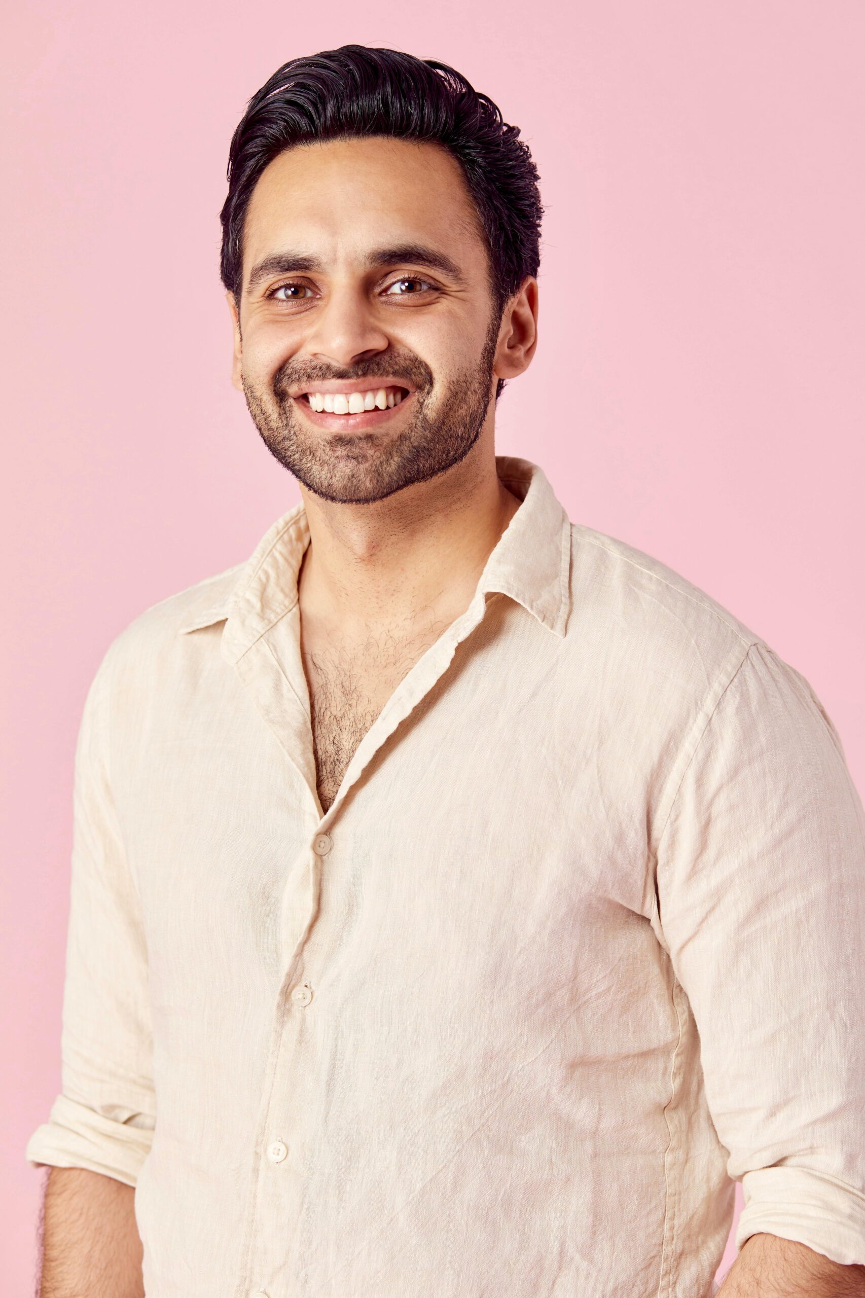 Portrait of a smiling man wearing a beige shirt against a pink background.